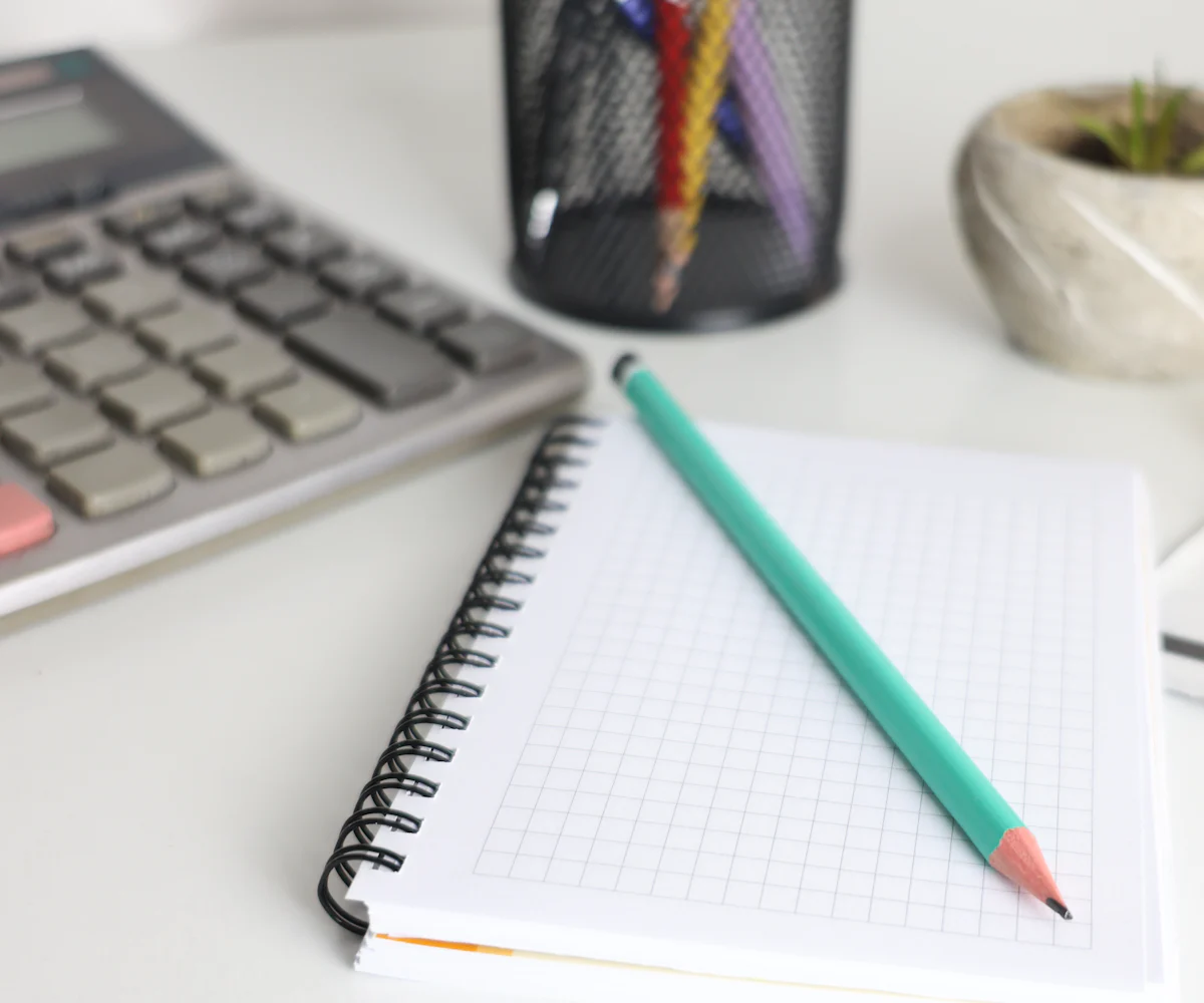 Calculadora, cuaderno cuadriculado y lápiz sobre un escritorio blanco