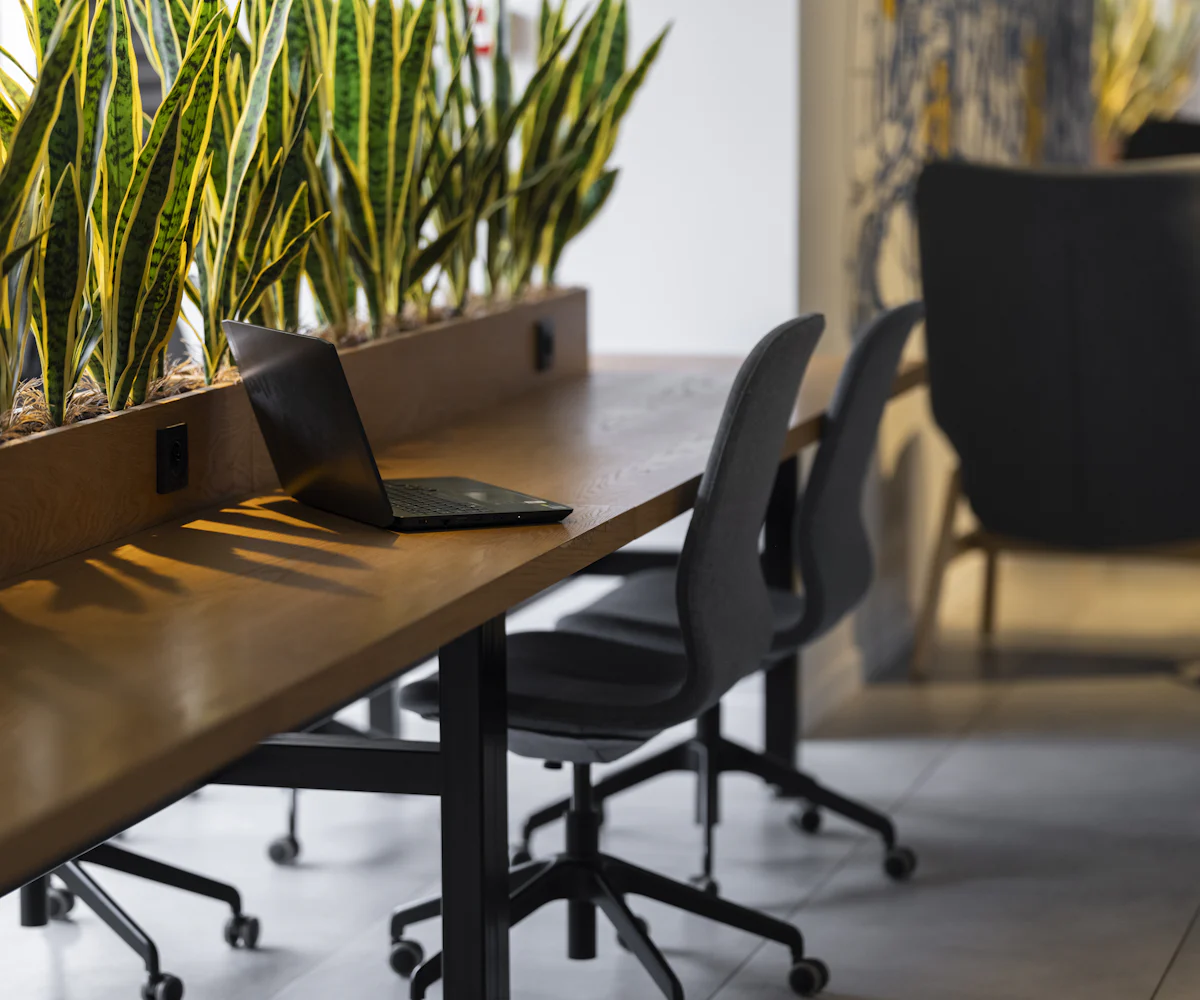 Puesto de trabajo vacío con un portátil cerrado, sillas de oficina y plantas